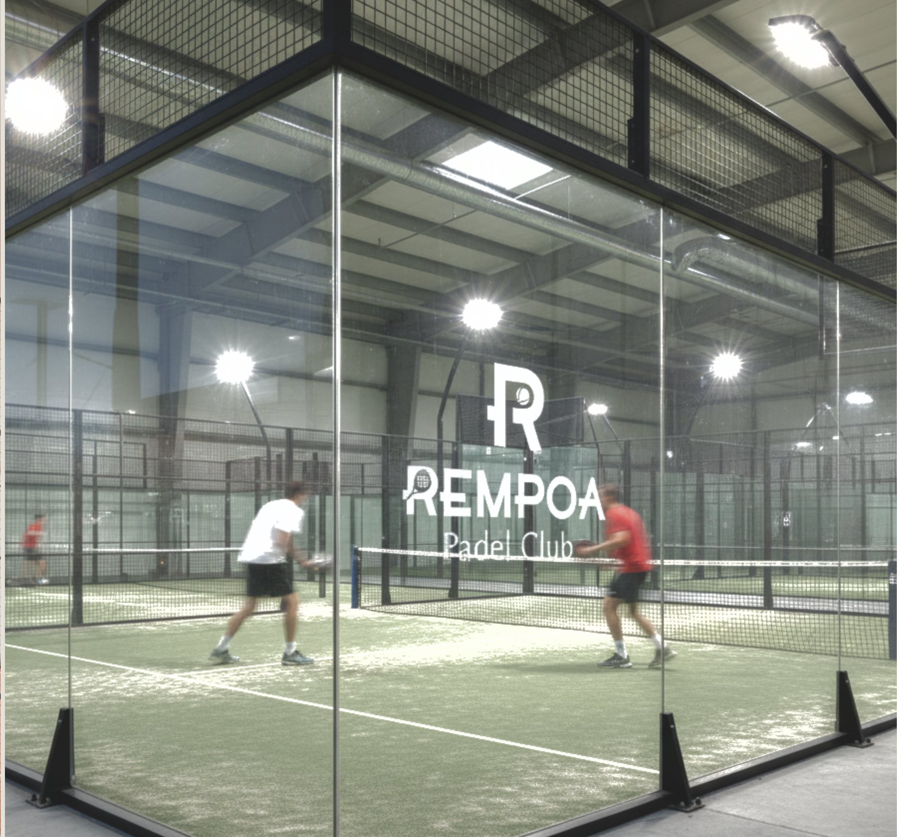 Lapangan padel indoor Rempoa Padel Club dengan dinding kaca dan dua pemain sedang bertanding